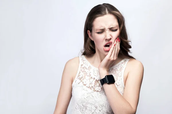 Portrait of beautiful woman with freckles and white dress and smart watch with tooth pain on silver gray background. healthcare and medicine concept. — Stock Photo, Image