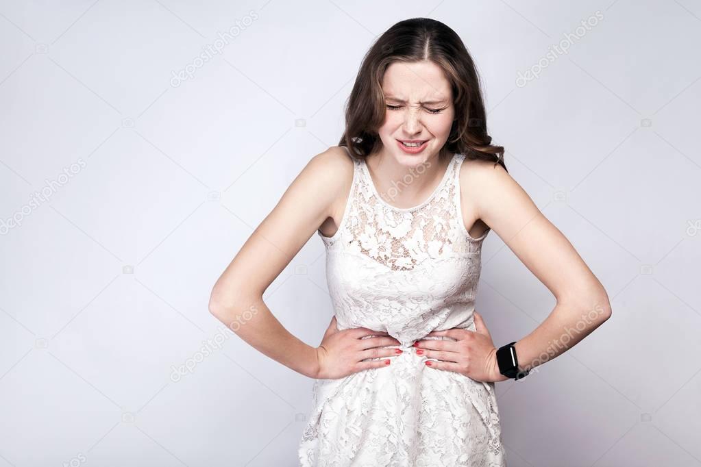 Portrait of beautiful woman with freckles and white dress and smart watch with stomach pain on silver gray background. healthcare and medicine concept.