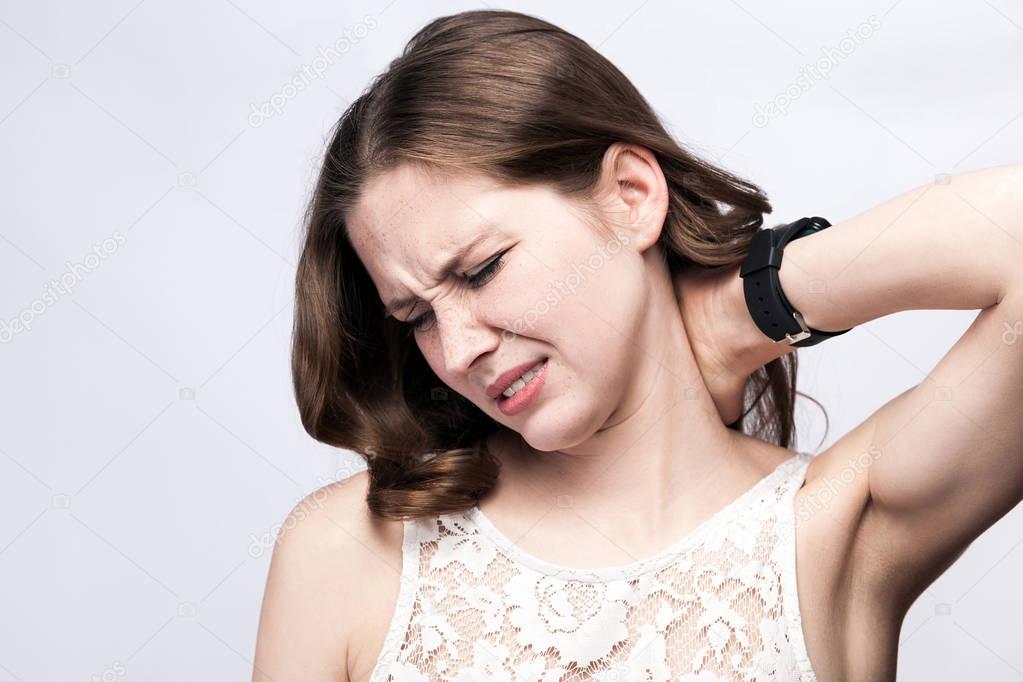 Portrait of beautiful woman with freckles and white dress and smart watch with neck pain on silver gray background. healthcare and medicine concept.