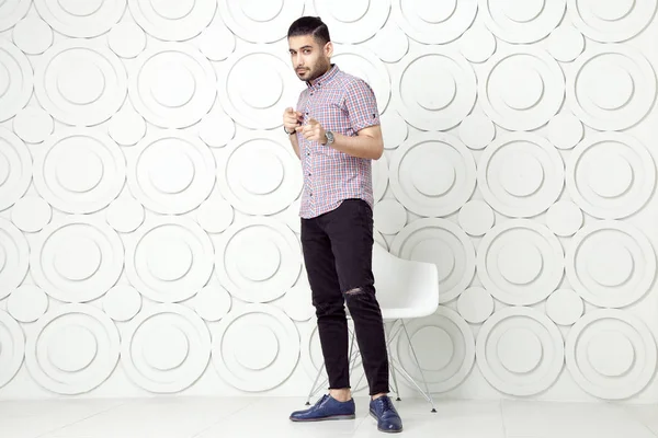 Mladý vousatý módní model v ležérní styl je představuje poblíž zdi pozadí bílý kruh. — Stock fotografie