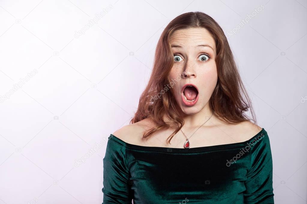 Portrait of shocked woman with freckles and classic green dress. studio shot on silver gray background. 