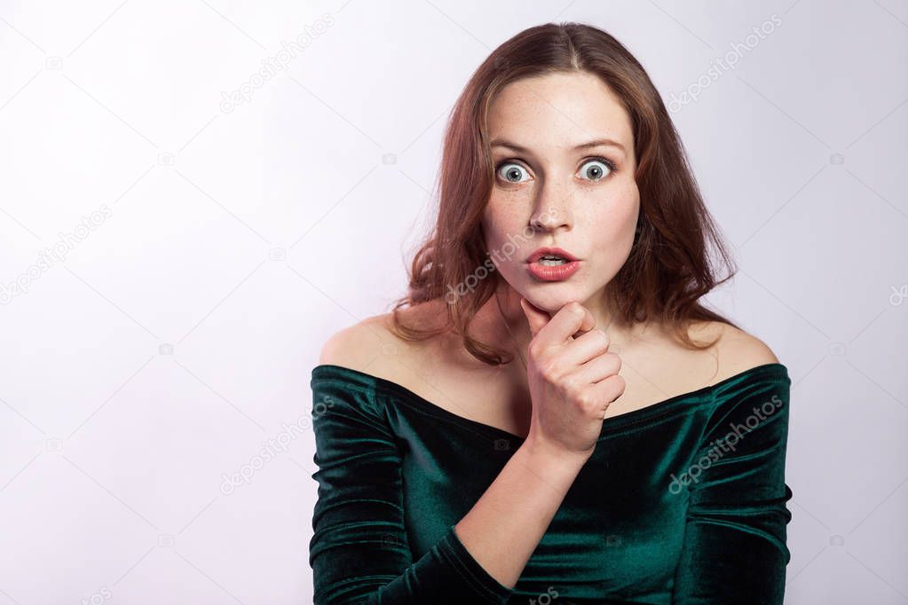 Portrait of shocked unbelieved woman with freckles and classic green dress. studio shot on silver gray background. 