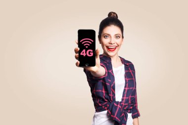 Kameraya bakarak ve 4 g gösterilen telefon tutarak rahat tarzı genç güzel kadın Internet telefon üzerinde görüntüler. bej renkli arka plan üzerinde atış stüdyo.