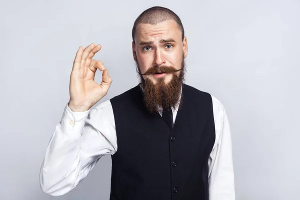 De acuerdo. Hombre de negocios guapo con barba y bigote manillar mirando a la cámara con signo Ok. plano de estudio, sobre fondo gris . — Foto de Stock