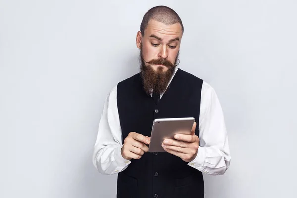 Bonito empresário com barba e bigode guiador segurando e usando tablet digital. estúdio tiro, em fundo cinza . — Fotografia de Stock
