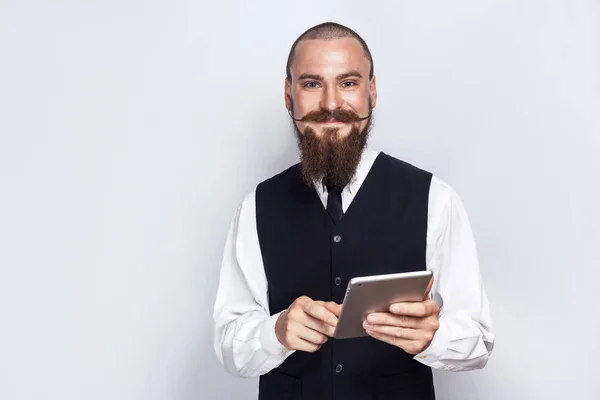 Beau homme d'affaires avec barbe et moustache de guidon tenant tablette numérique et regardant la caméra avec le visage souriant. plan studio, sur fond gris . — Photo