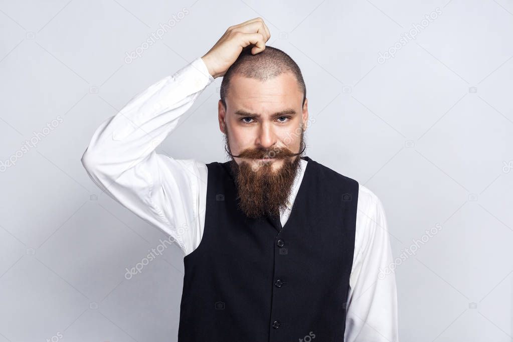 Thoughtful. Handsome businessman with beard and handlebar mustache looking at camera and thinking. studio shot, on gray background.