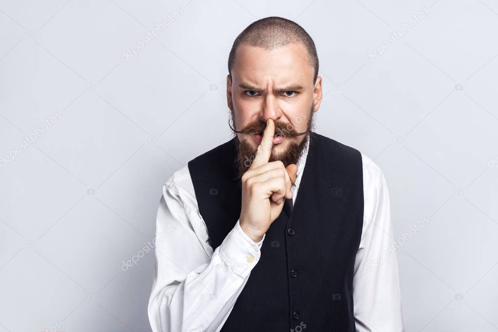 Shh, Handsome businessman with beard and handlebar mustache looking at camera with silent sing. studio shot, on gray background.