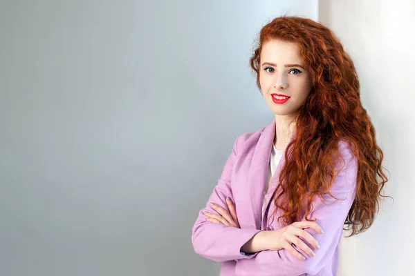 Retrato de exitosa mujer de negocios feliz hermosa con rojo - cabello castaño y maquillaje en traje rosa. mirando a la cámara con una sonrisa dentada, estudio filmado sobre fondo gris . — Foto de Stock