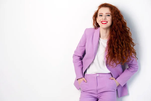 Retrato de exitosa mujer de negocios feliz hermosa con rojo - cabello castaño y maquillaje en traje rosa. mirando a la cámara con una sonrisa dentada, estudio filmado sobre fondo gris . — Foto de Stock