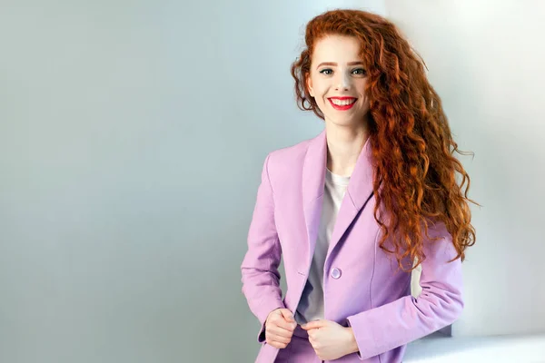 Portrait of successful happy beautiful business woman with red - brown hair and makeup in pink suit.  looking at camera with toothy smile. studio shot on gray background. — Stock Photo, Image