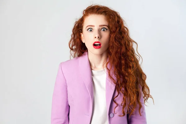 Retrato de impactada hermosa mujer de negocios con rojo - cabello castaño y maquillaje en traje rosa. mirando a la cámara, estudio filmado sobre fondo gris . —  Fotos de Stock