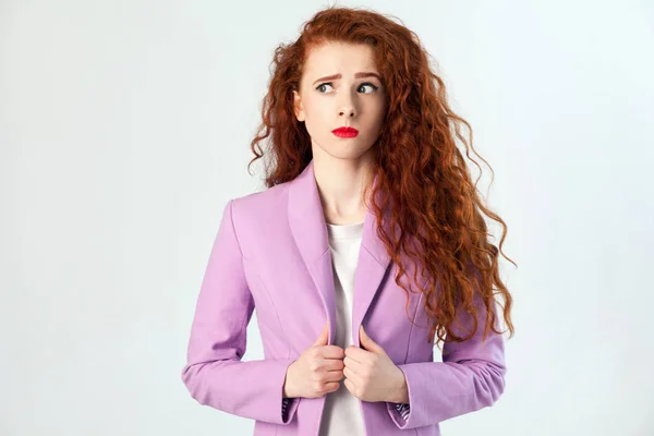 Porträt einer nachdenklichen schönen Geschäftsfrau mit rot-braunen Haaren und Make-up im rosa Anzug. Denken und Wegschauen, Studioaufnahme auf grauem Hintergrund. — Stockfoto