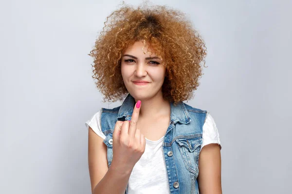 Retrato de louco encaracolado menina de raça mista em estilo casual está mostrando o dedo do meio e olhando para a câmera. estúdio filmado em fundo cinza claro . — Fotografia de Stock