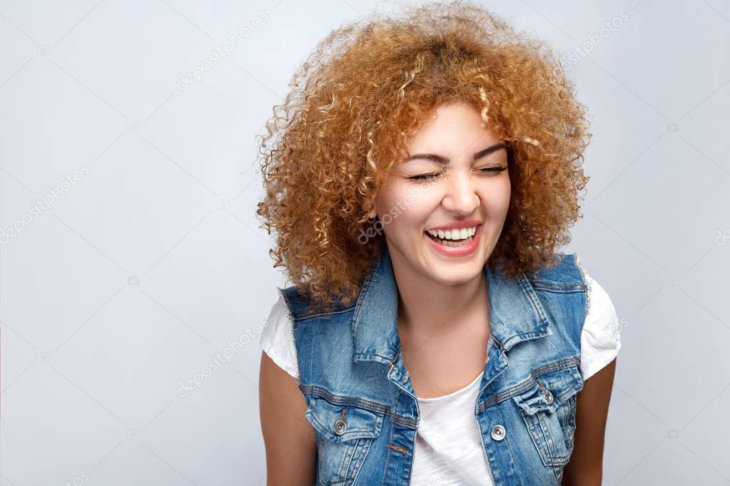 Portrait of beautiful happy curly mixed race girl in casual style is laughing. looking at camera. studio shot on light gray background. 
