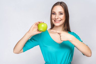 Çiller ve elma tutan ve parmak ile işaret yeşil elbise genç güzel kadın. 