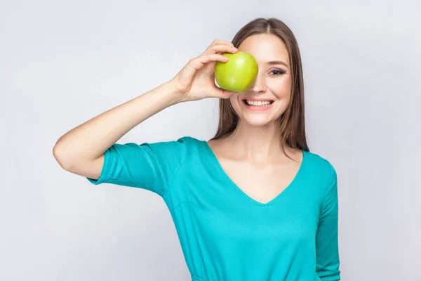 Jovem mulher bonita com sardas e vestido verde segurando maçã na frente de seus olhos e sorrindo  . — Fotografia de Stock