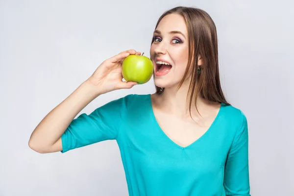 Jovem mulher bonita com sardas e vestido verde segurando maçã e comer olhando para a câmera — Fotografia de Stock