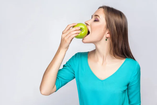 Young beautiful woman with freckles and green dress holding apple and eating with closed eyes. — Stock Photo, Image