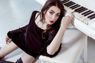 Siyah elbise ve bot ile dumanlı gözler makyaj ve katta oturan ve yakınındaki piyano ile poz saç moda model. Stüdyo vurdu.