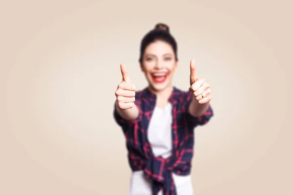 Young happy girl with casual style and bun hair thumbs up her finger, on beige blank wall with copy space looking at camera with toothy smile. focus on finger. — Stock Photo, Image