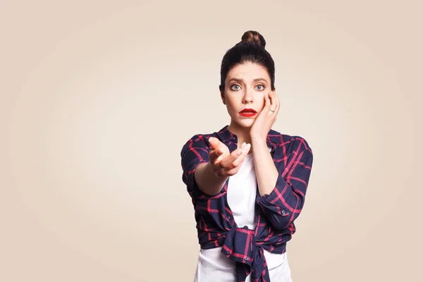 Ragazza spaventata con il nodo dei capelli del panino avendo paura e spaventato lo sguardo, tenendo la bocca aperta, toccando il viso e indicando la mano alla fotocamera . — Foto Stock