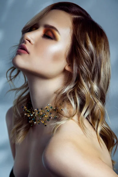 Beauty porträtt av beautful modell med makeup, färgade vawy frisyr och accessoarer på hennes hals. Studio skott på blå bakgrund. — Stockfoto