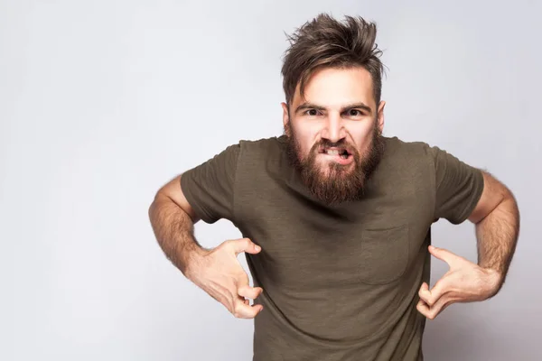 Ritratto di pazzo uomo barbuto arrabbiato con t-shirt verde scuro su sfondo grigio chiaro. studio girato . — Foto Stock