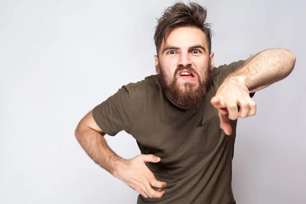 Ei, você! Retrato de homem barbudo furioso louco com t-shirt verde escuro contra fundo cinza claro. estúdio tiro . — Fotografia de Stock