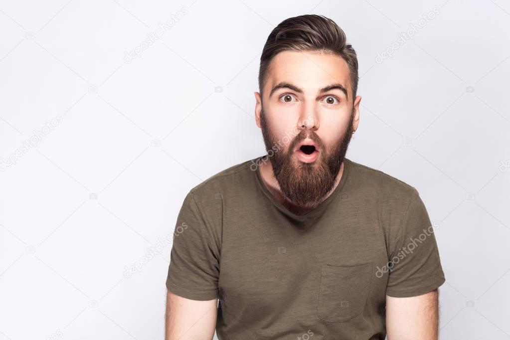 Portrait of surprised bearded man with dark green t shirt against light gray background. studio shot. 