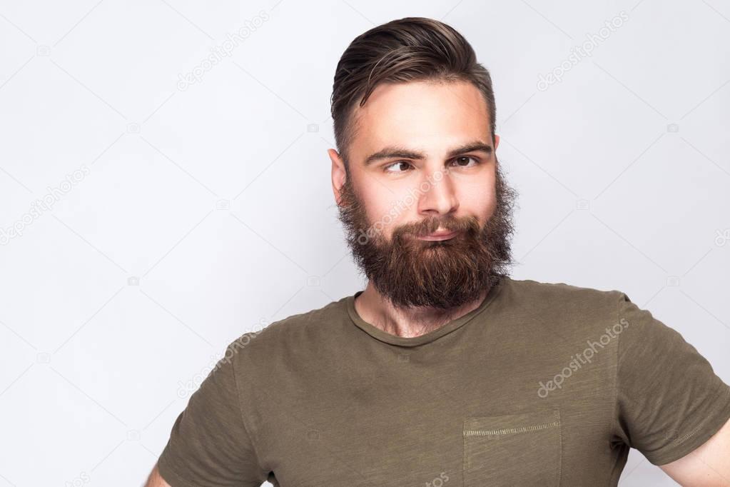 Portrait of crazy cross eyed bearded man with dark green t shirt against light gray background. studio shot. 