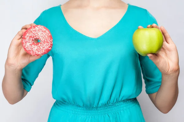 Mulher bonita em vestido verde segurando maçã e donut. estúdio filmado em fundo cinza claro — Fotografia de Stock