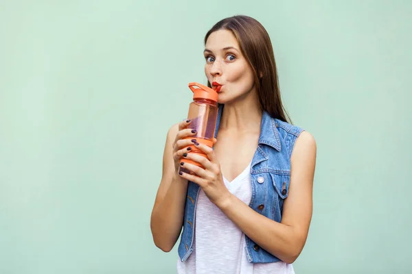 Menina bonita em estilo casual com garrafa de laranja de água no fundo verde . — Fotografia de Stock