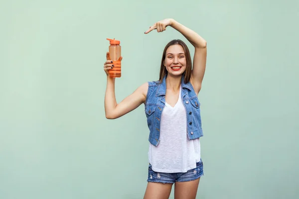 Menina bonita em estilo casual com garrafa de laranja de água no fundo verde . — Fotografia de Stock