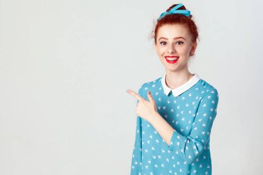 Şuna bak! Mutlu neşeli genç Kızıl saçlı beyaz kız beyaz boş duvar içerik veya promosyon bilgileri için kopya alanı gösteren saç topuz, onun parmağı işaret ile. Kapalı, stüdyo vurdu