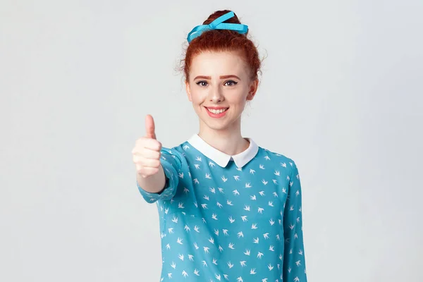 Молодая счастливая веселая рыжая девушка, показывающая большой палец и зубастую улыбку. Изолированная студия, снятая на сером фоне — стоковое фото