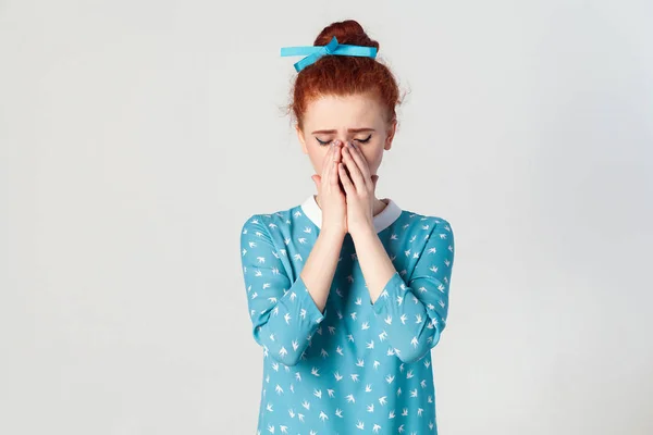 Portrait of unhappy, depressed and crying young caucasian girl with ginger hair feeling ashamed or sick, covering face with both hands, keeping eyes closed. Human face expressions and emotions concept. Isolated studio shot on gray background. — Stock Photo, Image