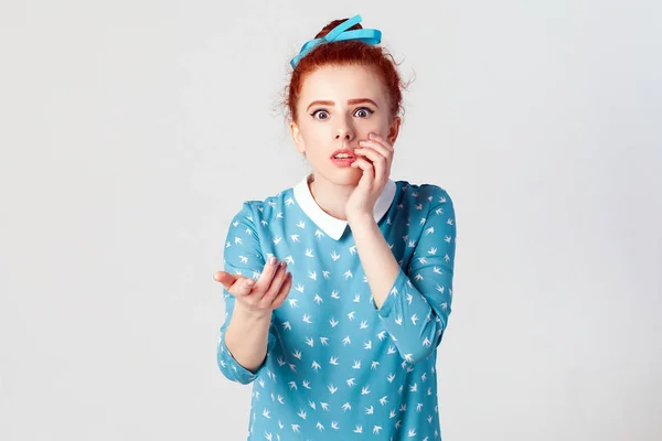 Human facial expressions, emotions and feelings. Beautiful redhead girl with hair knot having scared and frightened look, keeping mouth open, touching face and pointing hand at camera. Film effect. Focus on face. Isolated studio shot on gray backgrou