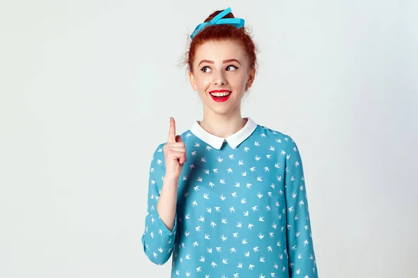 The beautiful redhead girl got the idea and she raised her finger up. Isolated studio shot on gray background — Stock Photo, Image