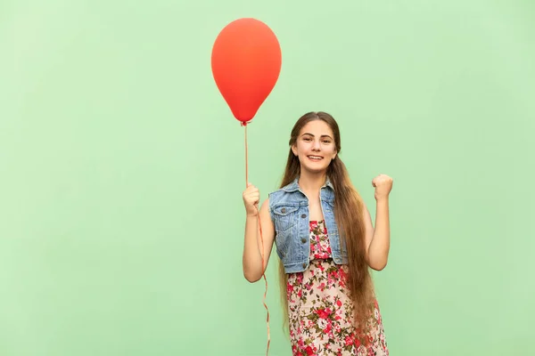 Haar winn! De mooie blonde tiener met rode ballonnen op een groene achtergrond. Geïsoleerde studio opname — Stockfoto