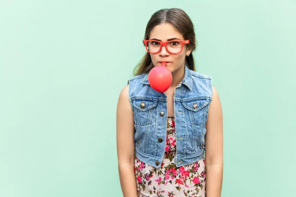 Gelukkig meisje blazen ballonnen voor verjaardagsfeestje, grappig kijken naar de camera op een lichtgroene achtergrond. Indoor studio shoot — Stockfoto