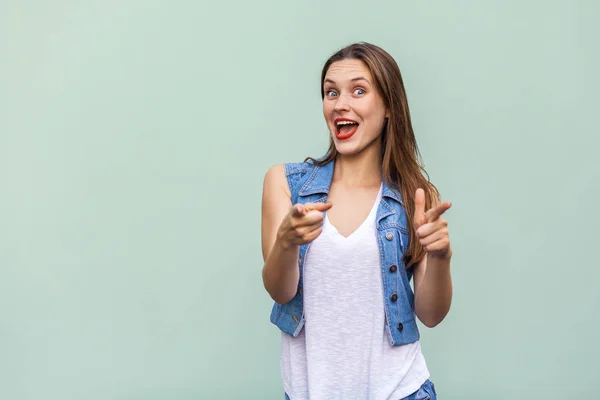 Happy cheerful teenage girl with freckles, casual style white t shirt and jeans jacket looking at camera, pointing two fingers at camera having joyful look, enjoying good day and free time indoors. Studio shot — Stock Photo, Image