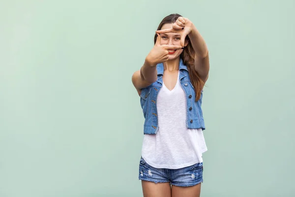 Creatieve jonge volwassen vrouw met sproeten, waardoor een frame gebaar met haar vingers als ze lijkt door te visualiseren van een project of de samenstelling van een foto. Indoor studio opname op lichtgroene achtergrond — Stockfoto