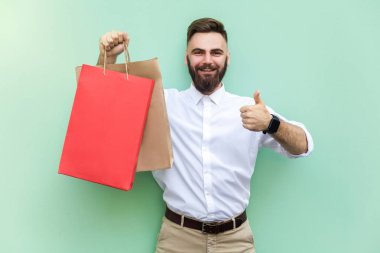 Online alışveriş veya bankacılık. Genç Yetişkin işadamı başparmak yukarı ve kamera ve dişlek gülümseme bakıyor. Kapalı, stüdyo vurdu
