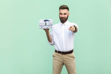 Kamera işaret ve bir hediye kutusu tutan genç yetişkin sakallı adam. Açık yeşil renkli stüdyo vurdu