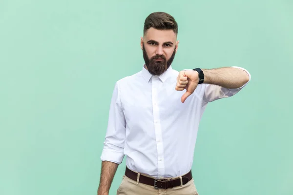 Retrato de hombre barbudo insatisfecho con pulgares hacia abajo y camisa blanca sobre fondo verde claro. Captura de estudio . — Foto de Stock