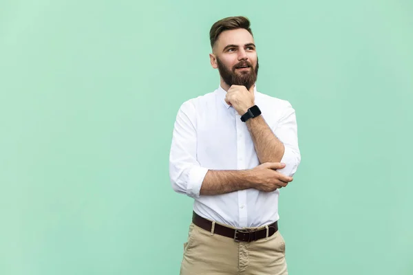 Продуманий бородатий бізнесмен, дивлячись геть, стоячи на світло-зеленій стіні. Студійний знімок — стокове фото