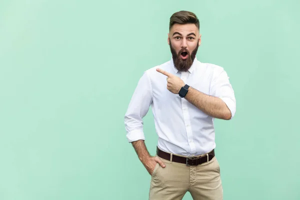 Wow! Knappe jonge volwassen man met baard in shoked. Weg te wijzen terwijl staande geïsoleerd op lichtgroene achtergrond — Stockfoto