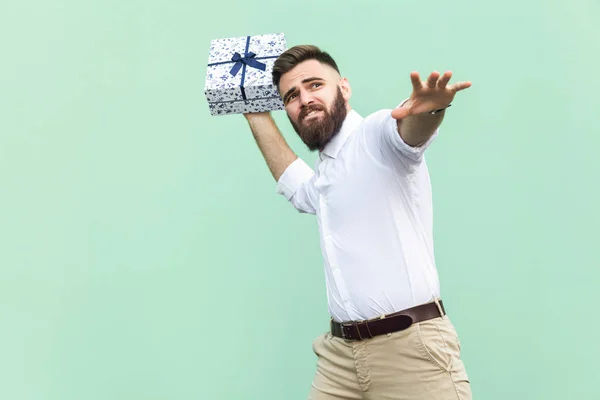 Prendi il tuo regalo! Giovane uomo adulto oscillato e vuole buttare via la confezione regalo, isolato su sfondo verde chiaro. Studio girato — Foto Stock