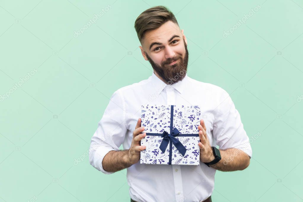 Gift with love. Interesting bearded young adult man with a gift box on light green background. Studio shot